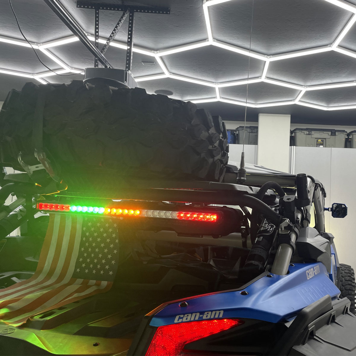Can-Am vehicle with a mounted spare tire and LED light bar, featuring an American flag, inside a modern garage with hexagonal lighting, emphasizing organized and functional garage spaces.