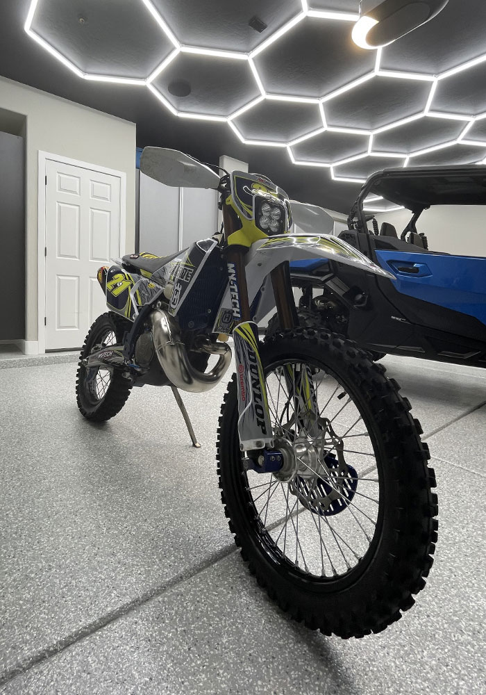 Motorcycle parked in a modern garage with hexagonal LED ceiling lights, showcasing Gear Up Garage's transformation of spaces into functional environments.