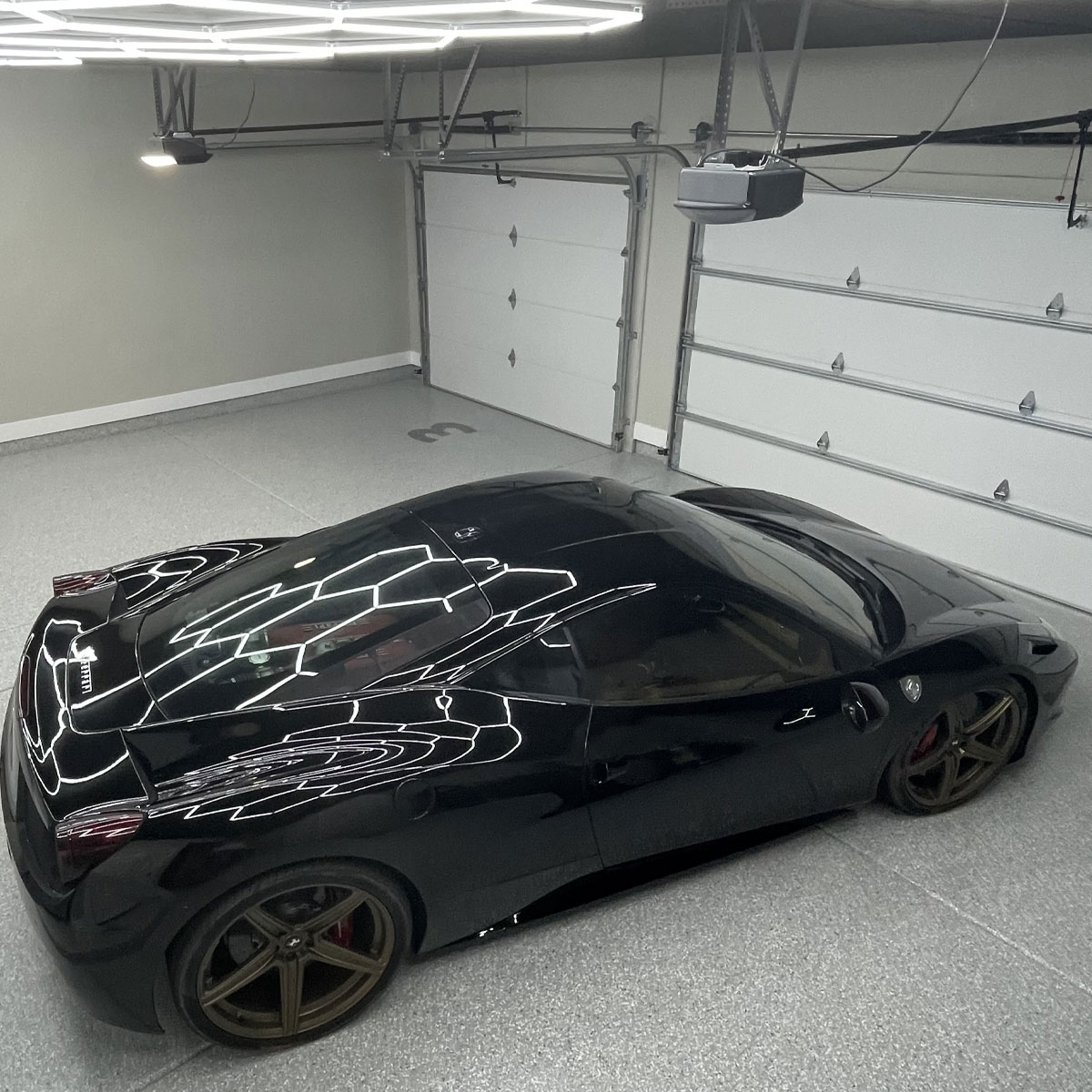 Black sports car parked in a modern garage with epoxy flooring and custom lighting, showcasing the sleek design and craftsmanship of the space.