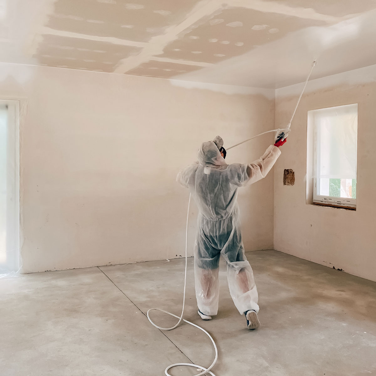 Person in protective gear spray painting a garage interior, showcasing the transformation process for enhanced functionality and aesthetics.